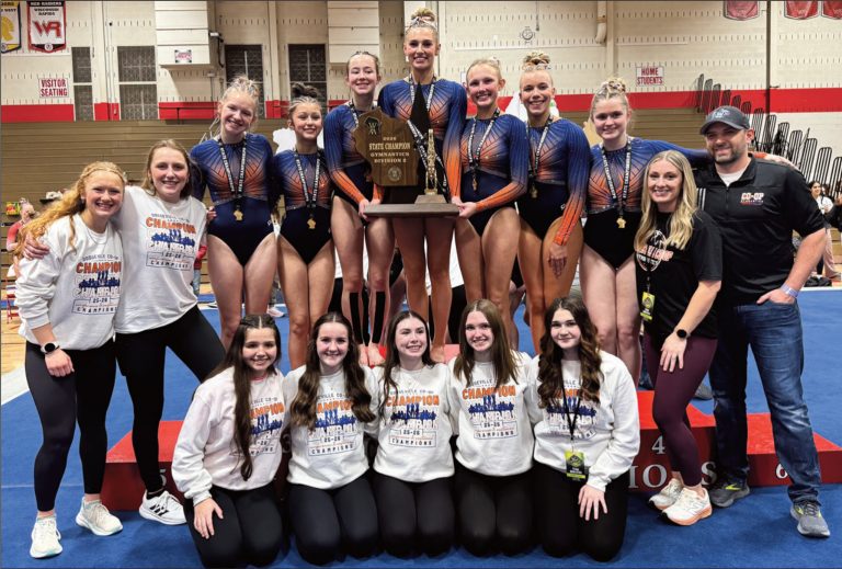 The Dodgeville Co-Op Gymnastics Team stands on the podium with its WIAA Division 2 State Championship trophy